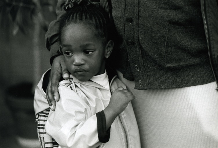 A little girl being shielded by the caring hand of her mother.