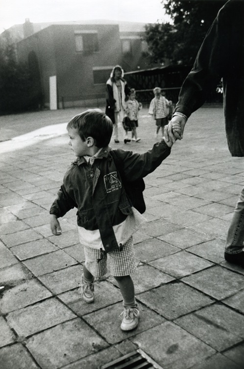 A boy holding the hand of his father. He's looking back into the sunshine, realising the long lazy summer is over.