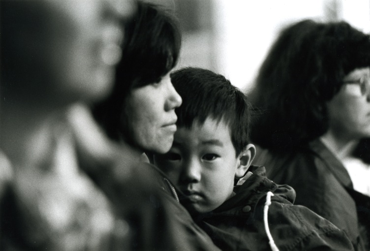 A mum looking into the distance, her son - cuddled up close to her - looking straight in the camera. He looks a little anxious.